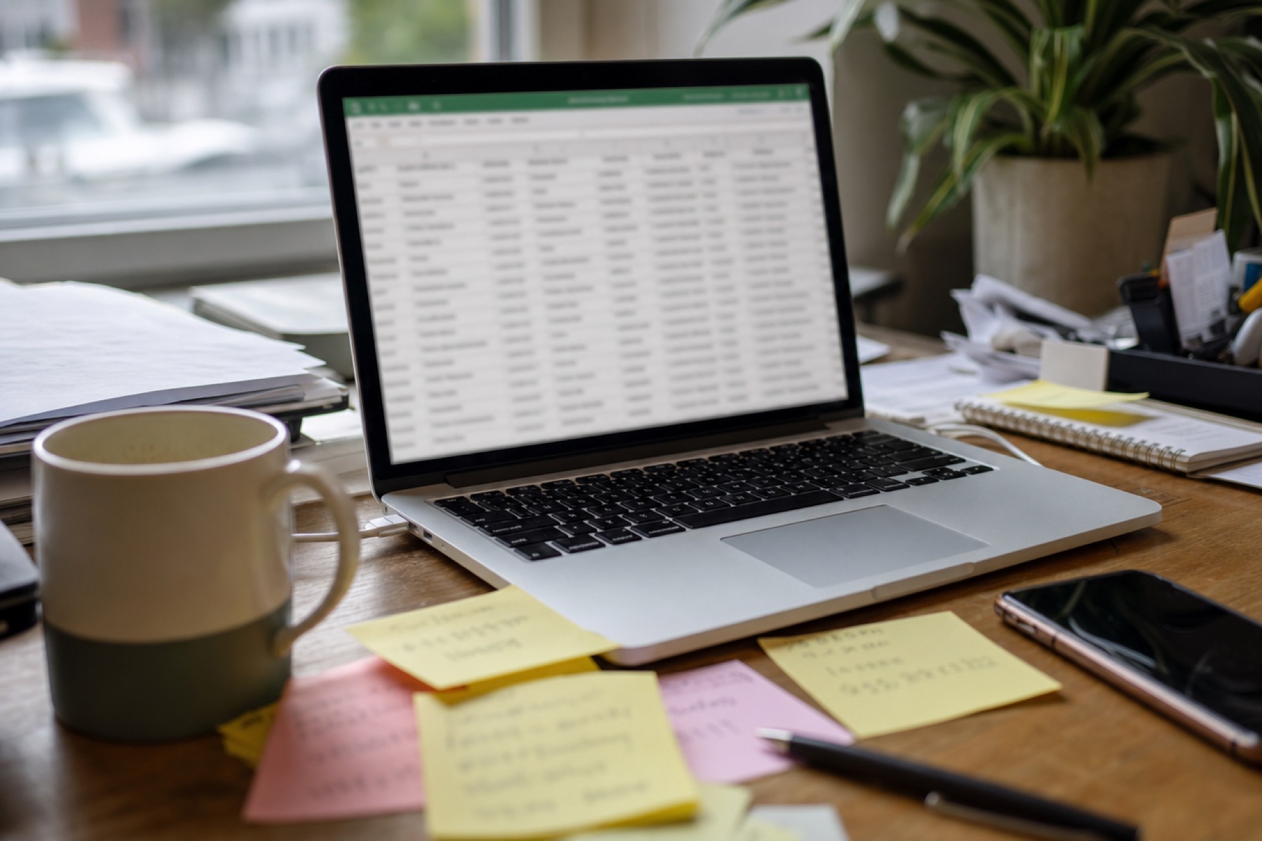 Laptop open to a contact spreadsheet beside sticky notes and a phone